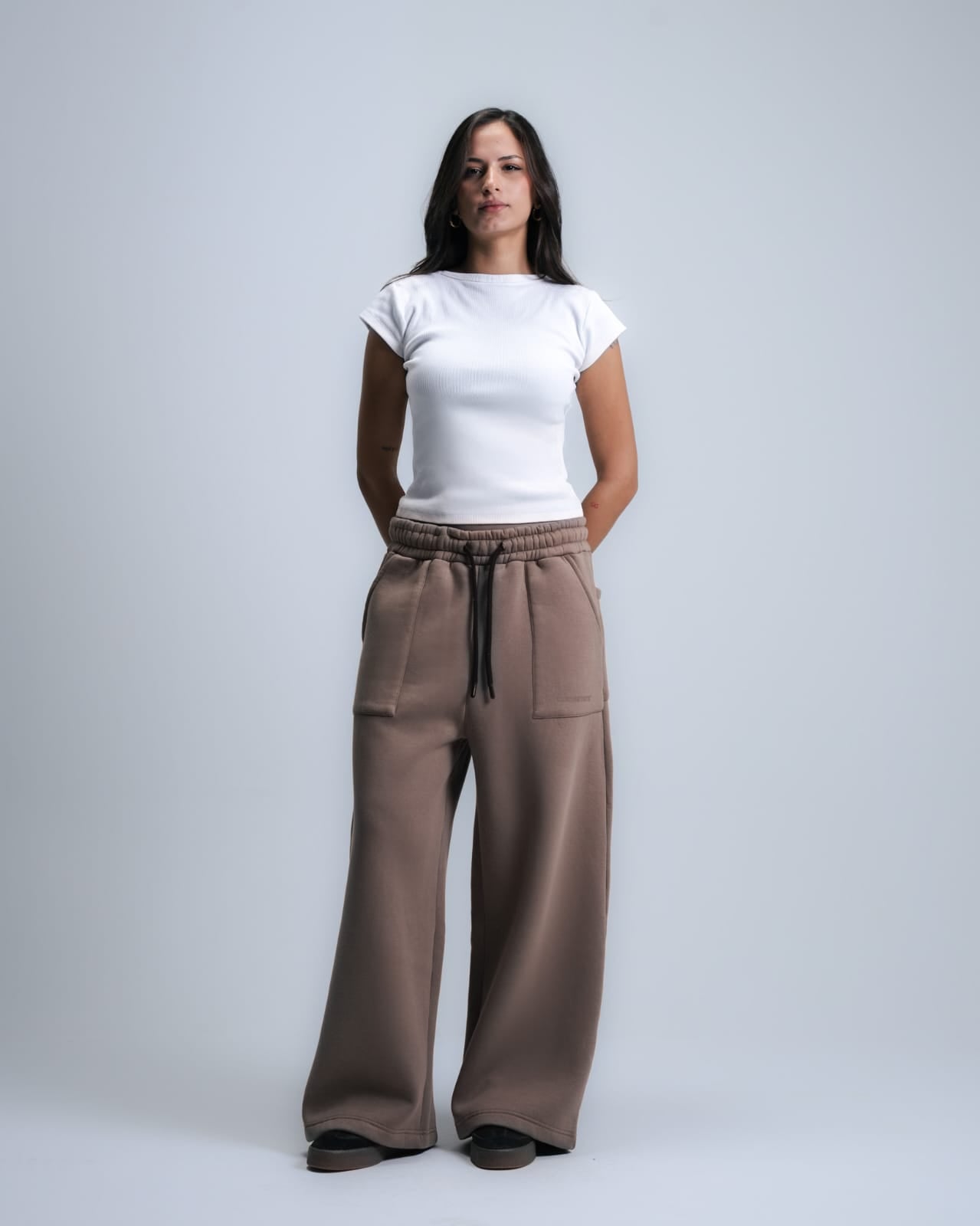 Woman wearing a white top and brown wide-leg pants on a plain background