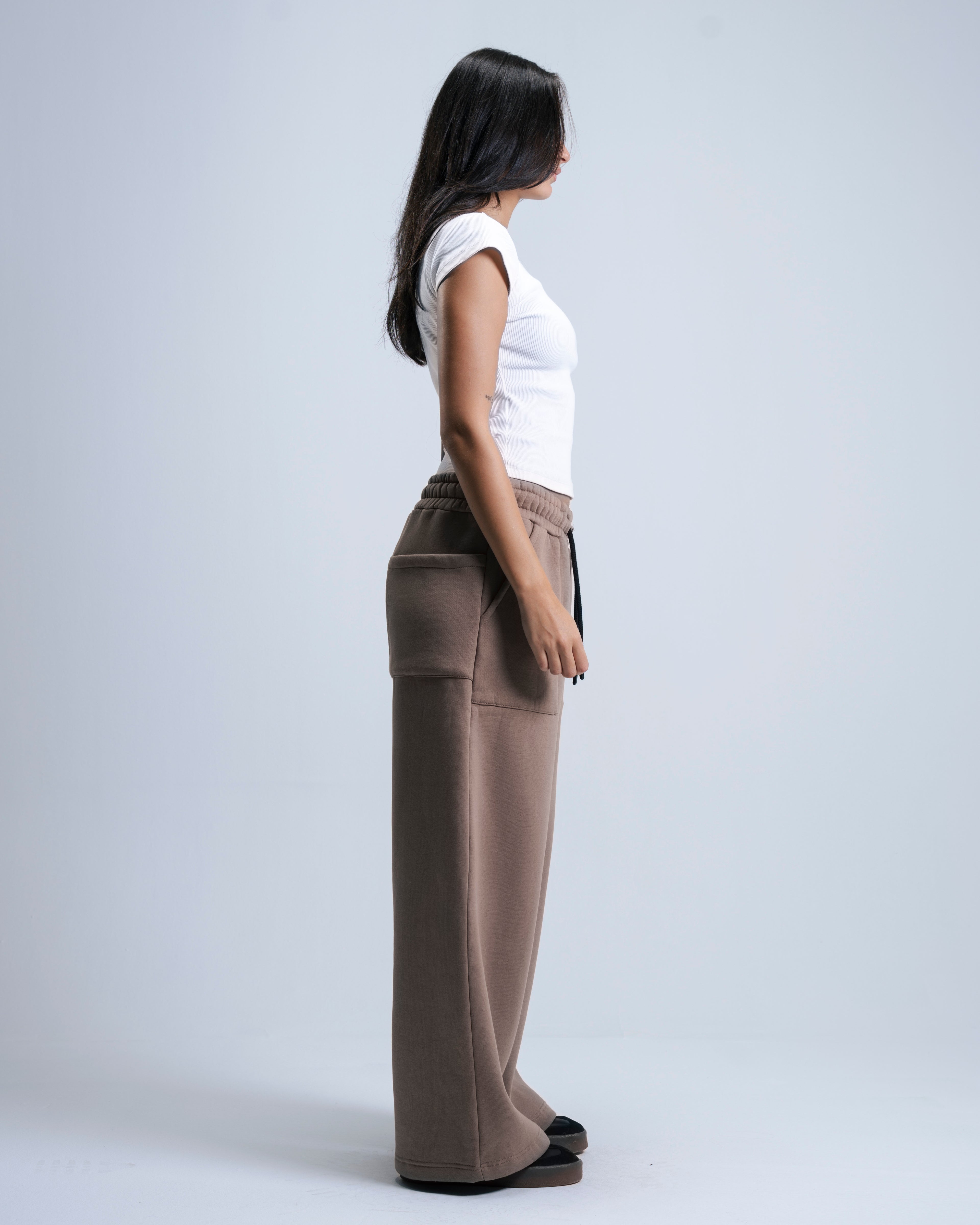 Woman wearing brown wide-leg pants and a white top on a light gray background