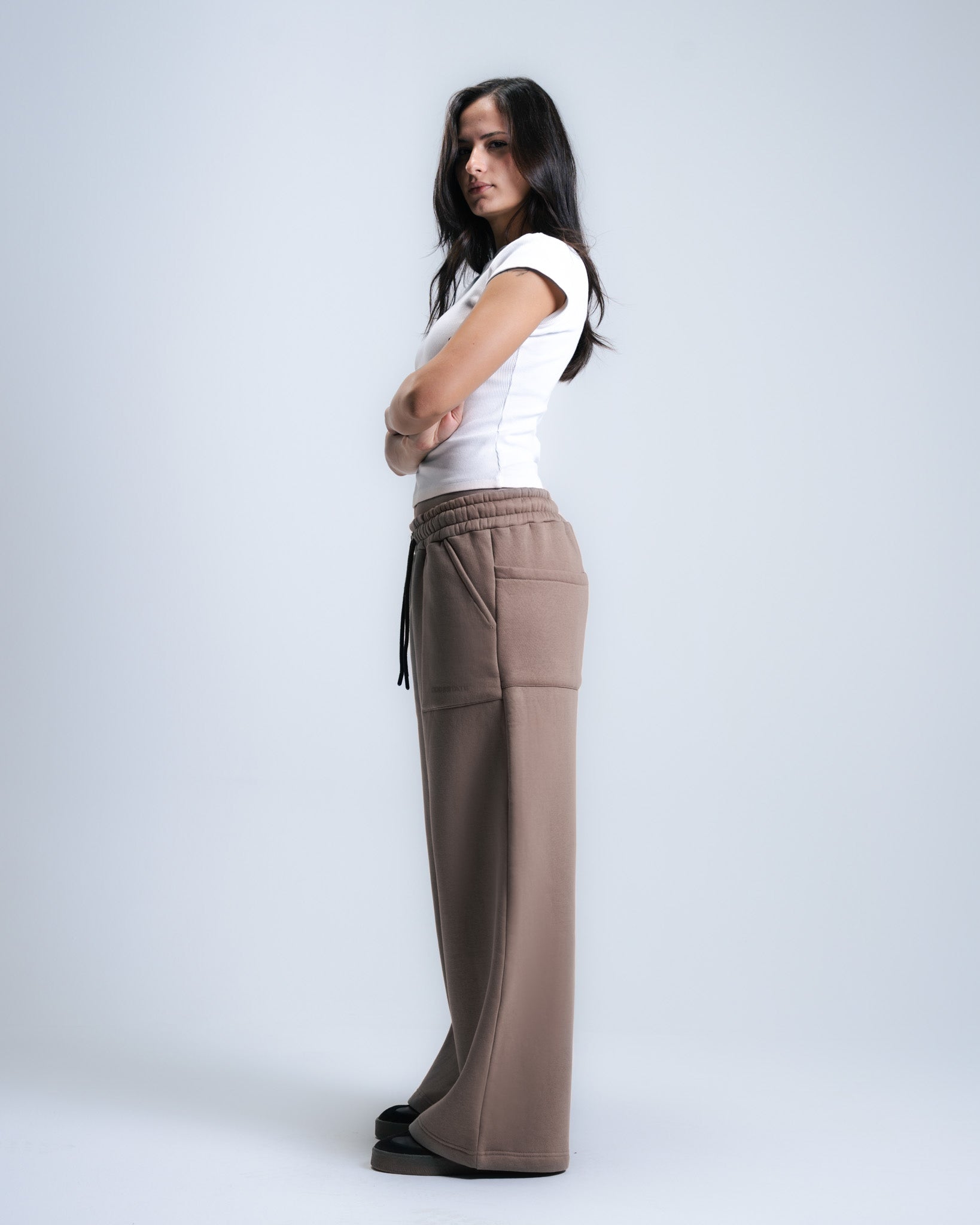 Woman wearing a white top and brown pants on a plain background