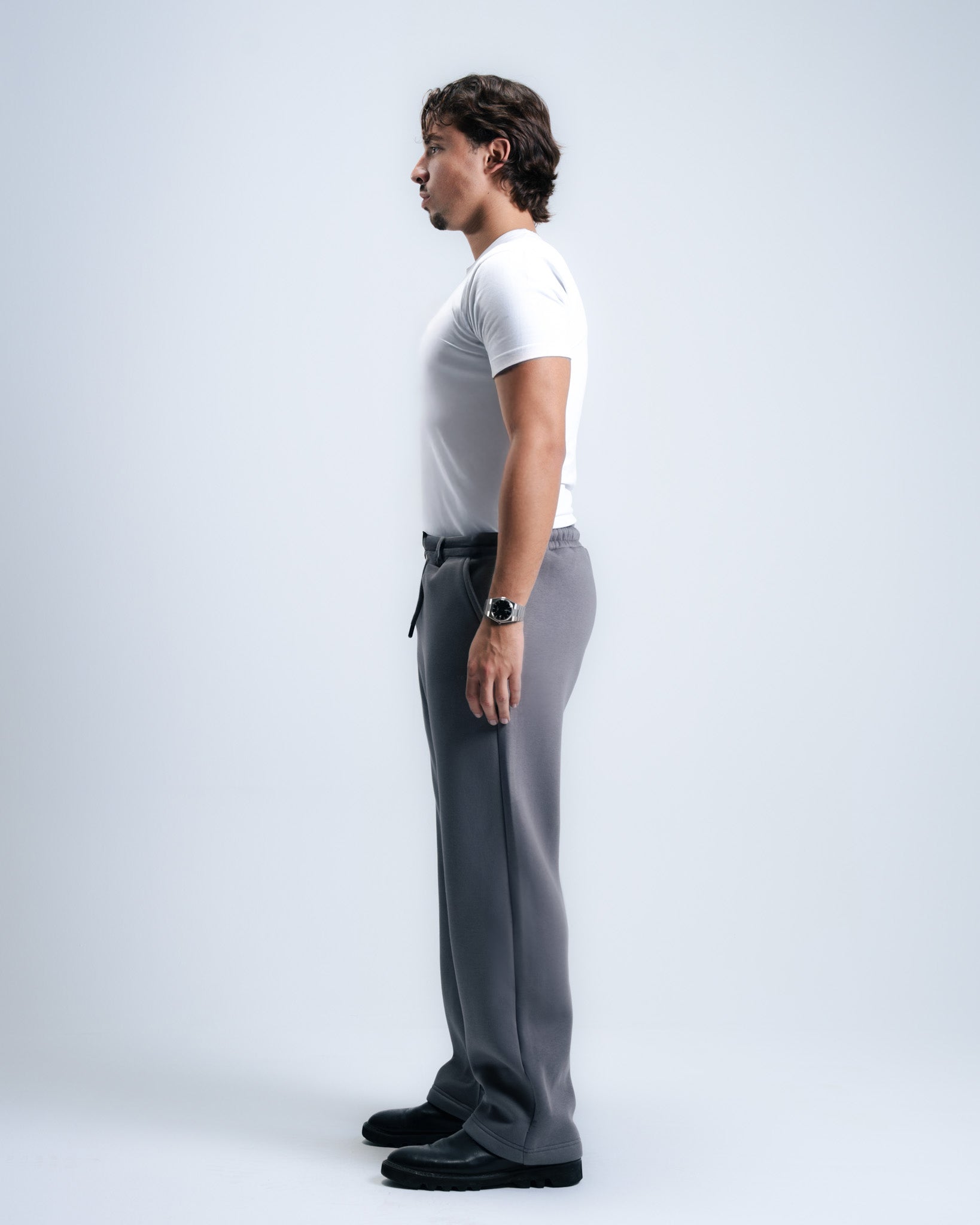 Man wearing a white t-shirt and gray pants on a light gray background