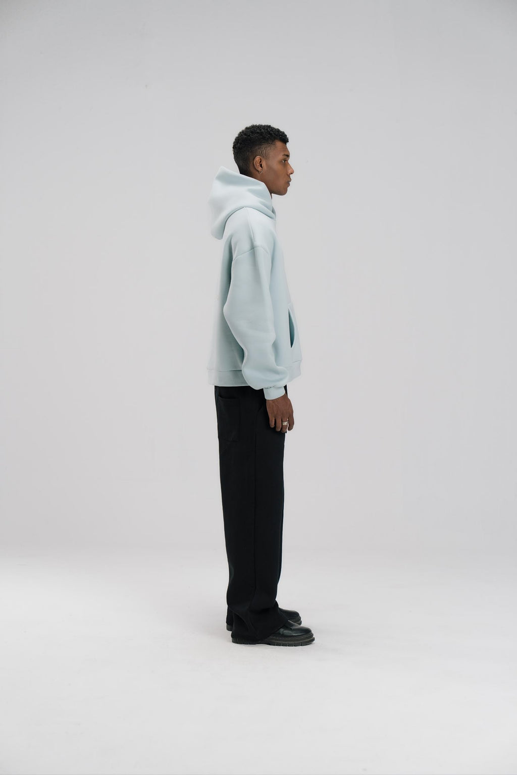 Person wearing a light blue hoodie and black pants on a white background