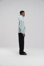 Person wearing a light blue hoodie and black pants on a white background