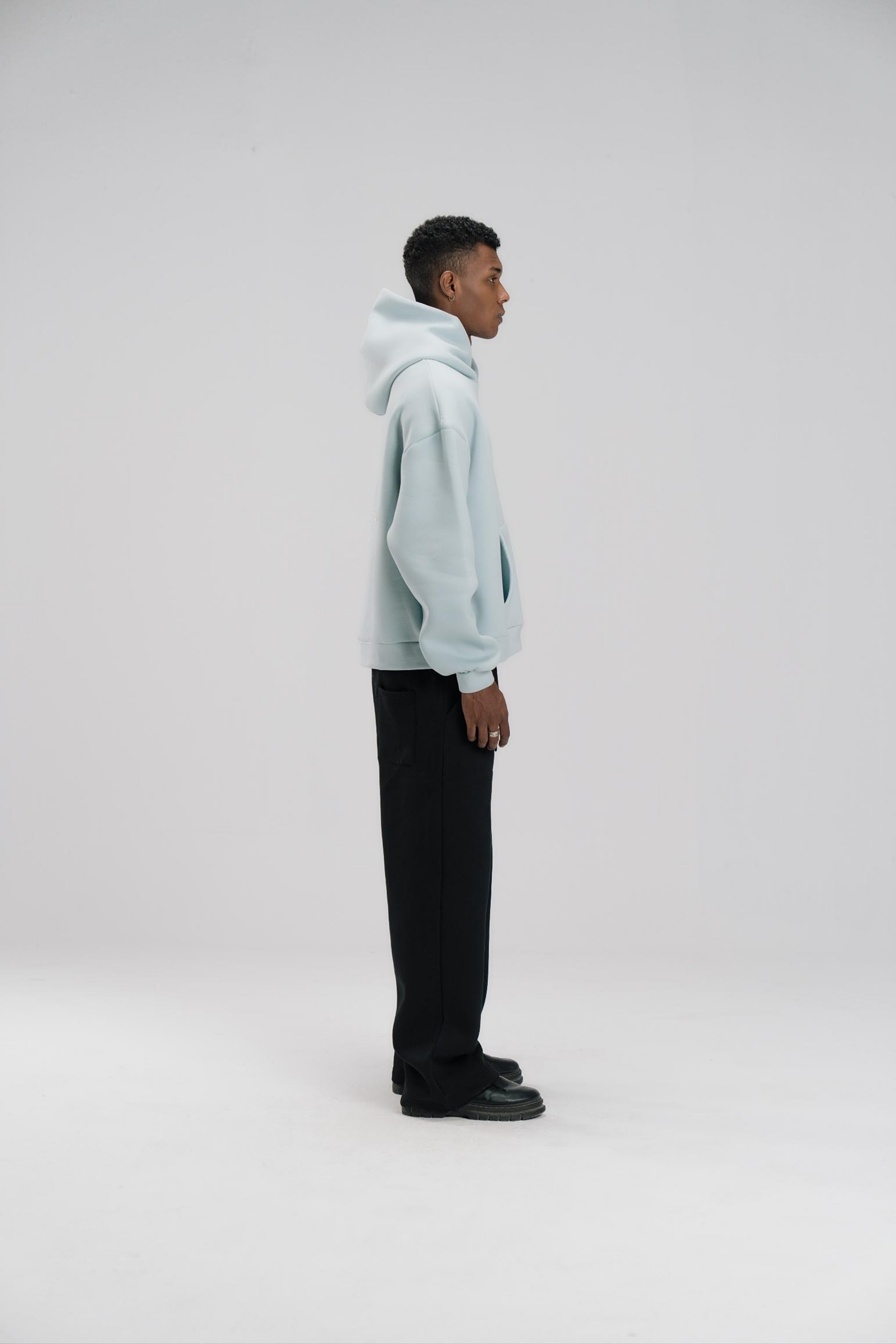 Person wearing a light blue hoodie and black pants on a white background