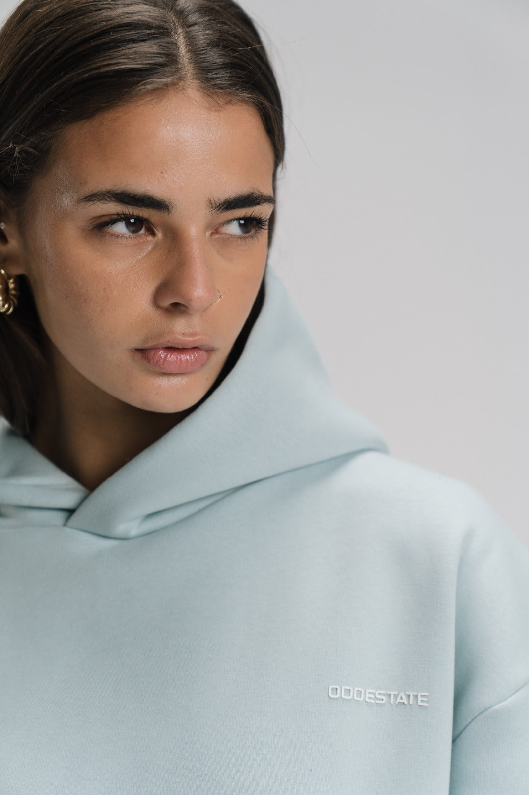 Person wearing a light blue hoodie with 'ODDESTATE' branding on a plain background