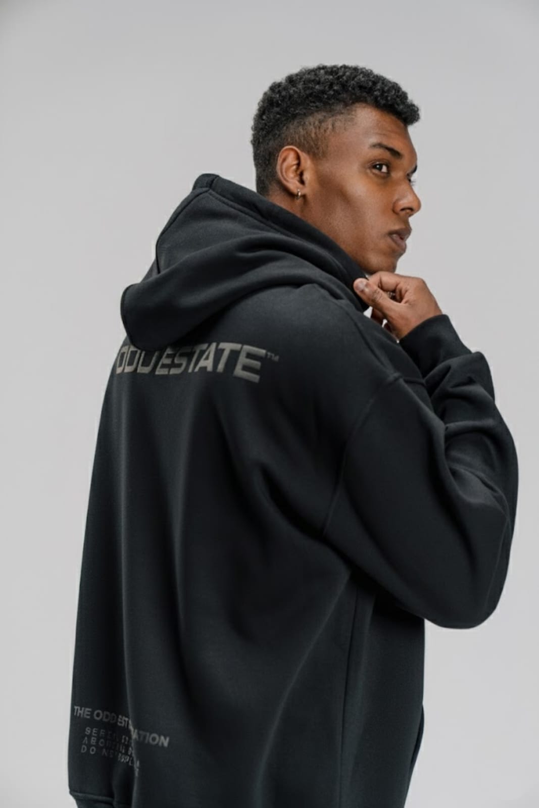 Person wearing a black hoodie with text on the back against a plain background