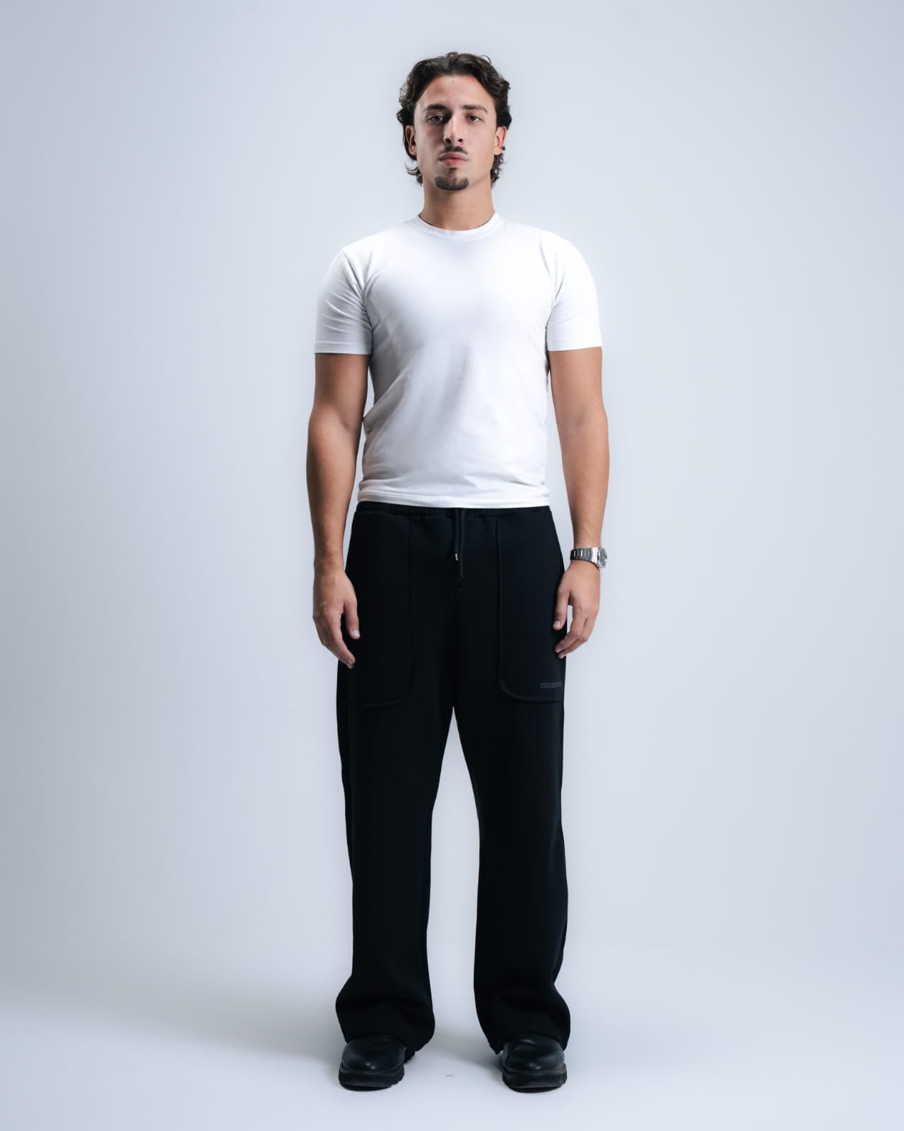 Man wearing a white t-shirt and black pants on a plain background