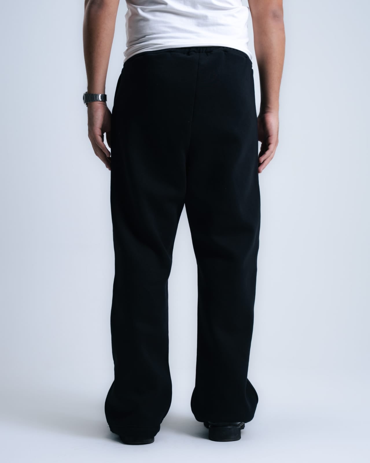 Person wearing black pants and a white shirt on a plain background