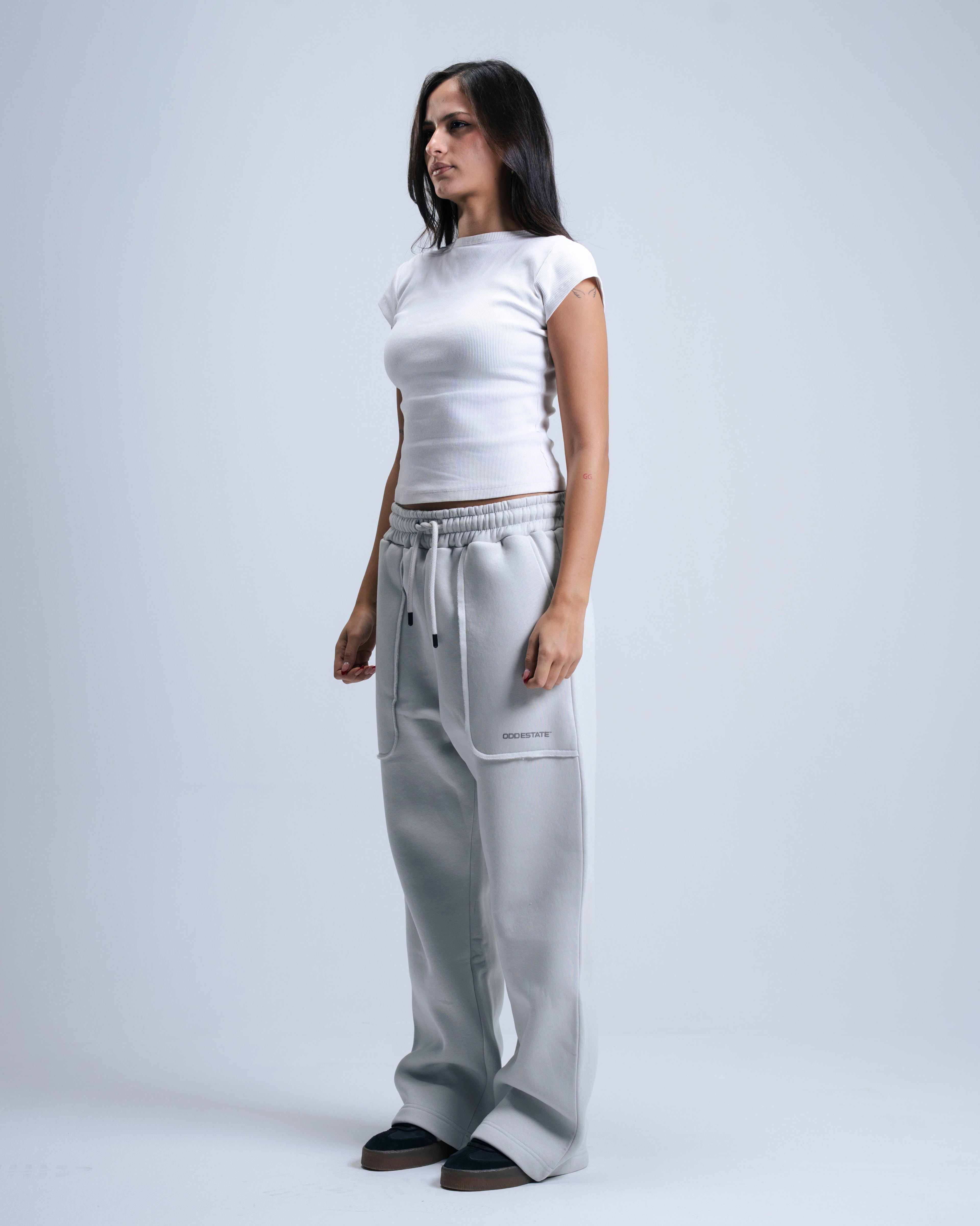 Woman wearing a white top and gray pants on a plain background
